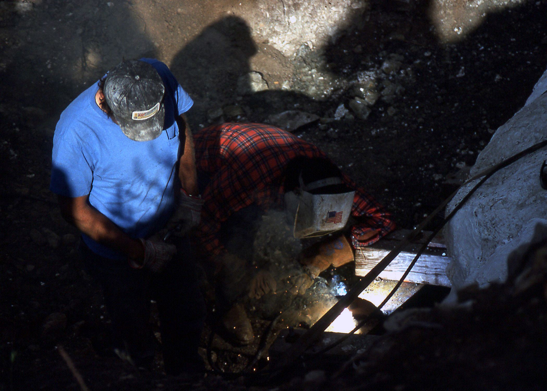 Color photo of a person welding bolts to the supports of the stegosaurus fossil plaster jacket.
