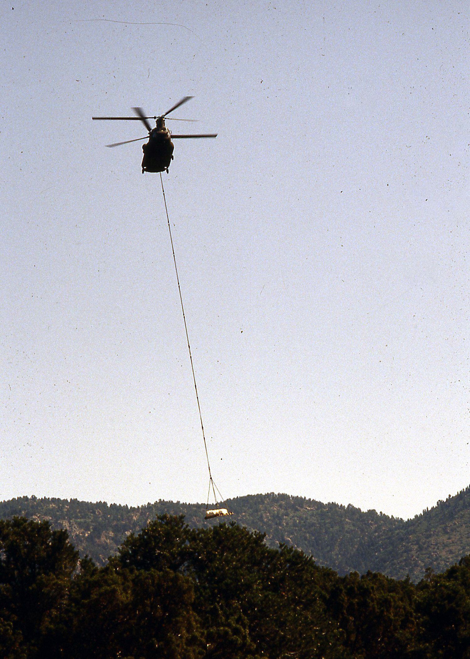 Color photo of Chinook helicopter flying with a stegosaurus fossil attached by cable. Circa 1992.