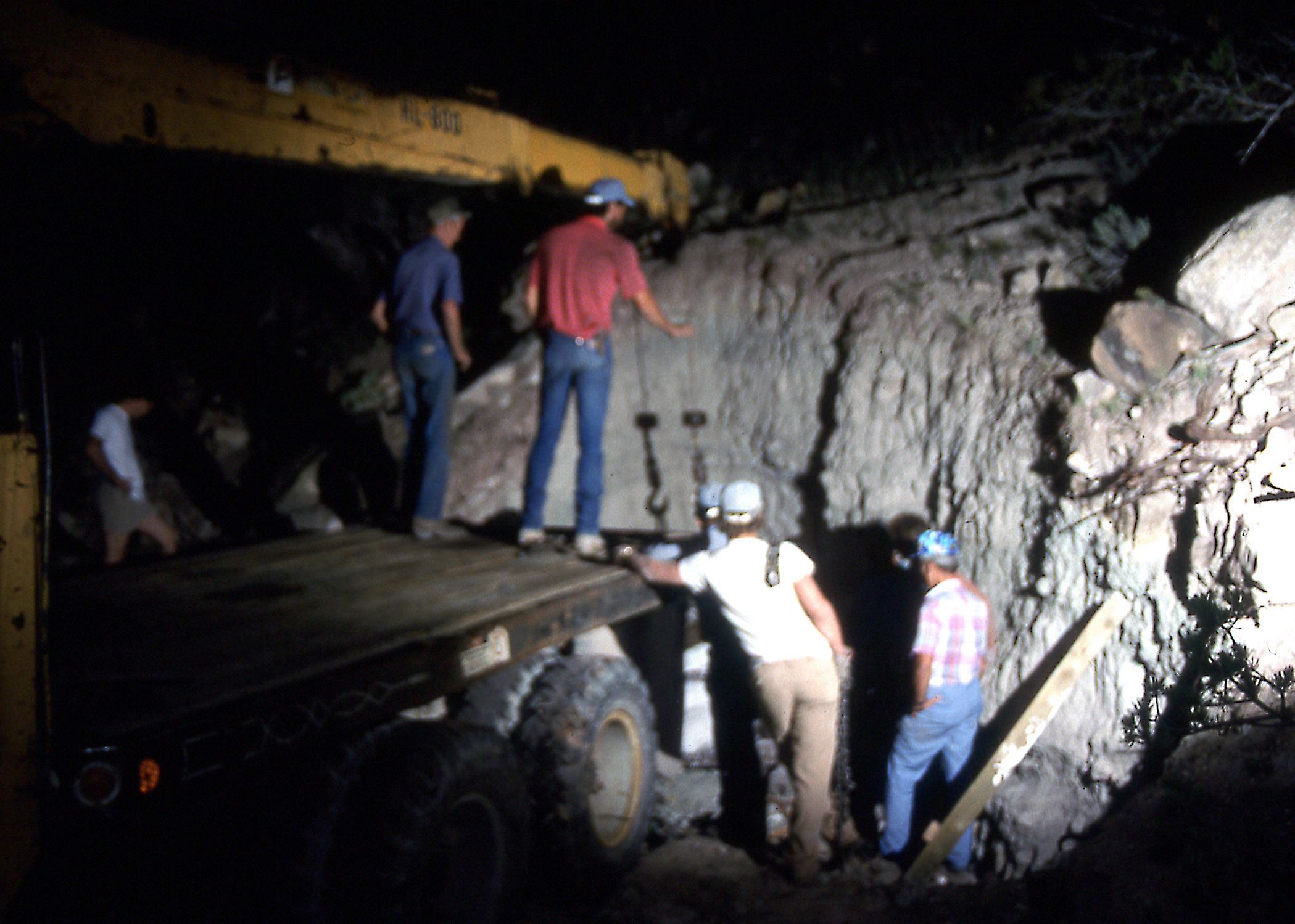 Color photo of men working at night preparing to extract the tail section of a stegosaurus fossil.